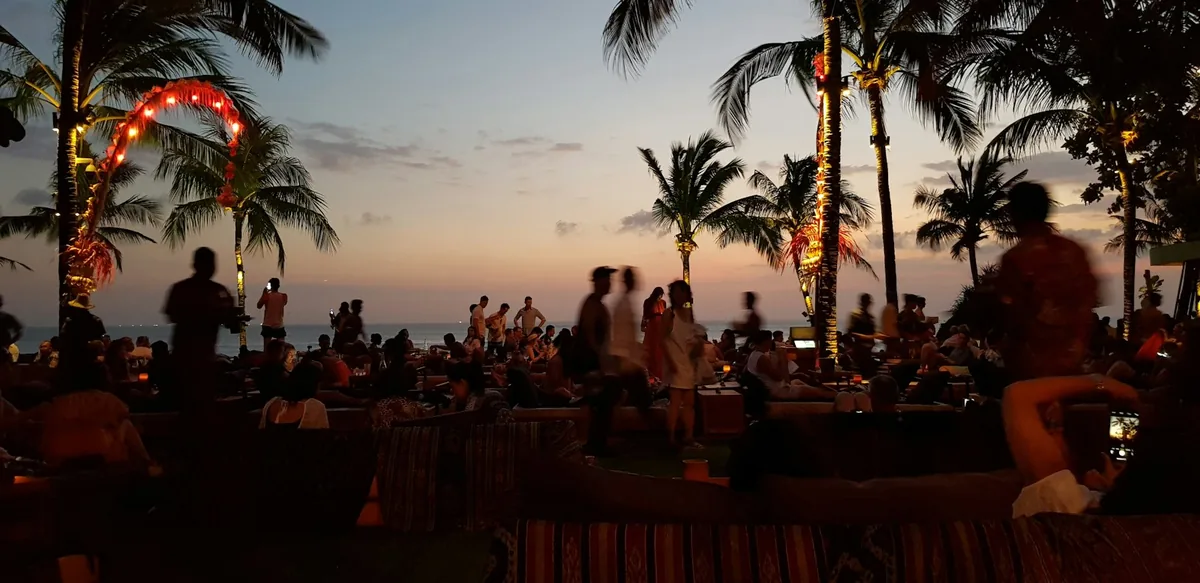 Silhouettes of people gathering on a beach with palm trees at sunset after a surf session