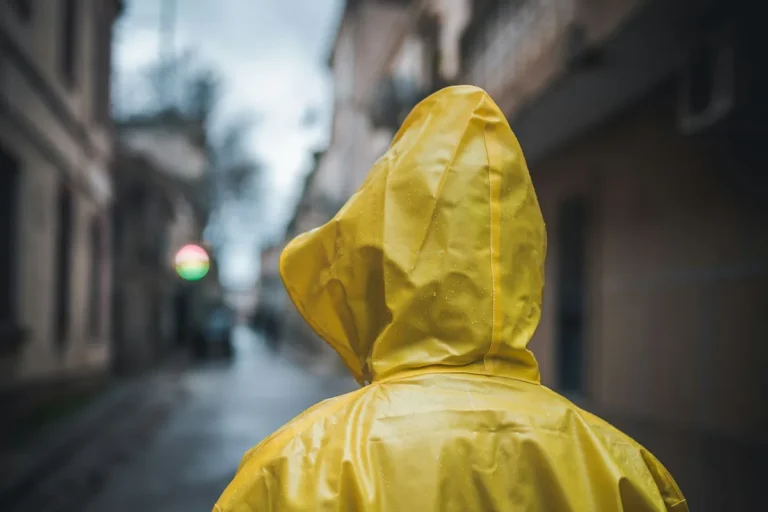 A person in a yellow raincoat with the hood up walking down a wet street