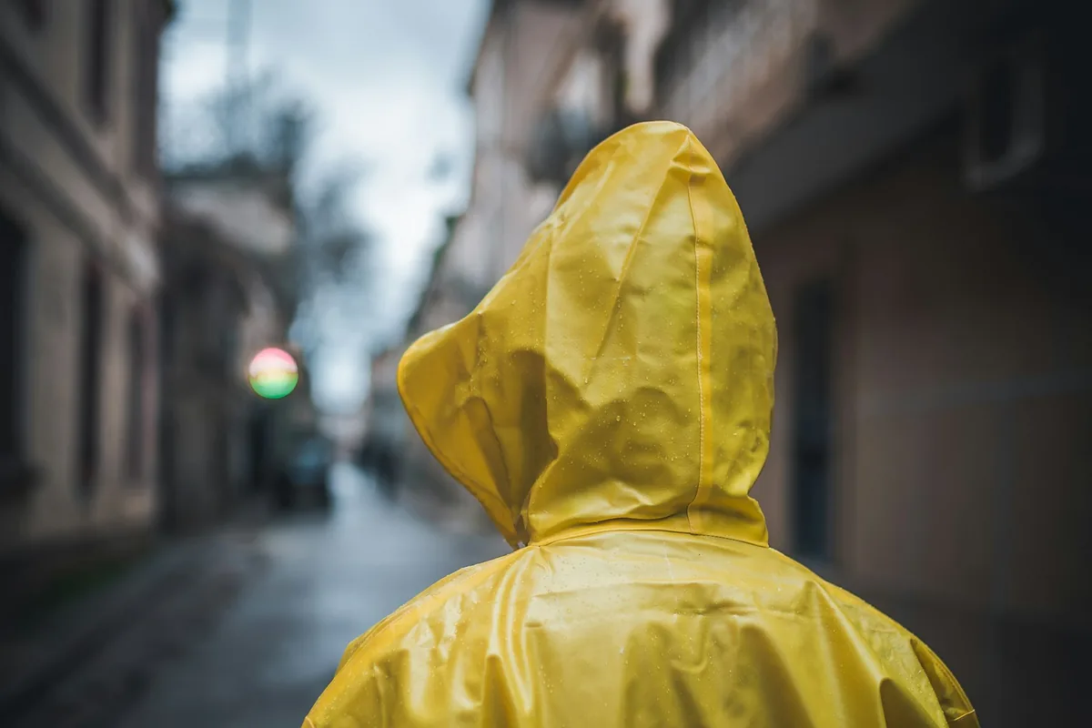 A person in a yellow raincoat with the hood up walking down a wet street