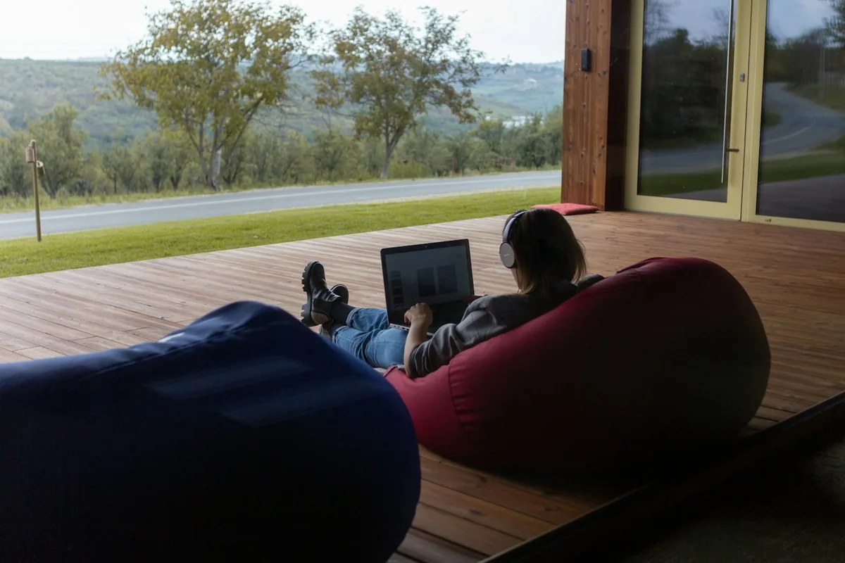 Een persoon op een zitzak die buiten op een laptop werkt met uitzicht op heuvels