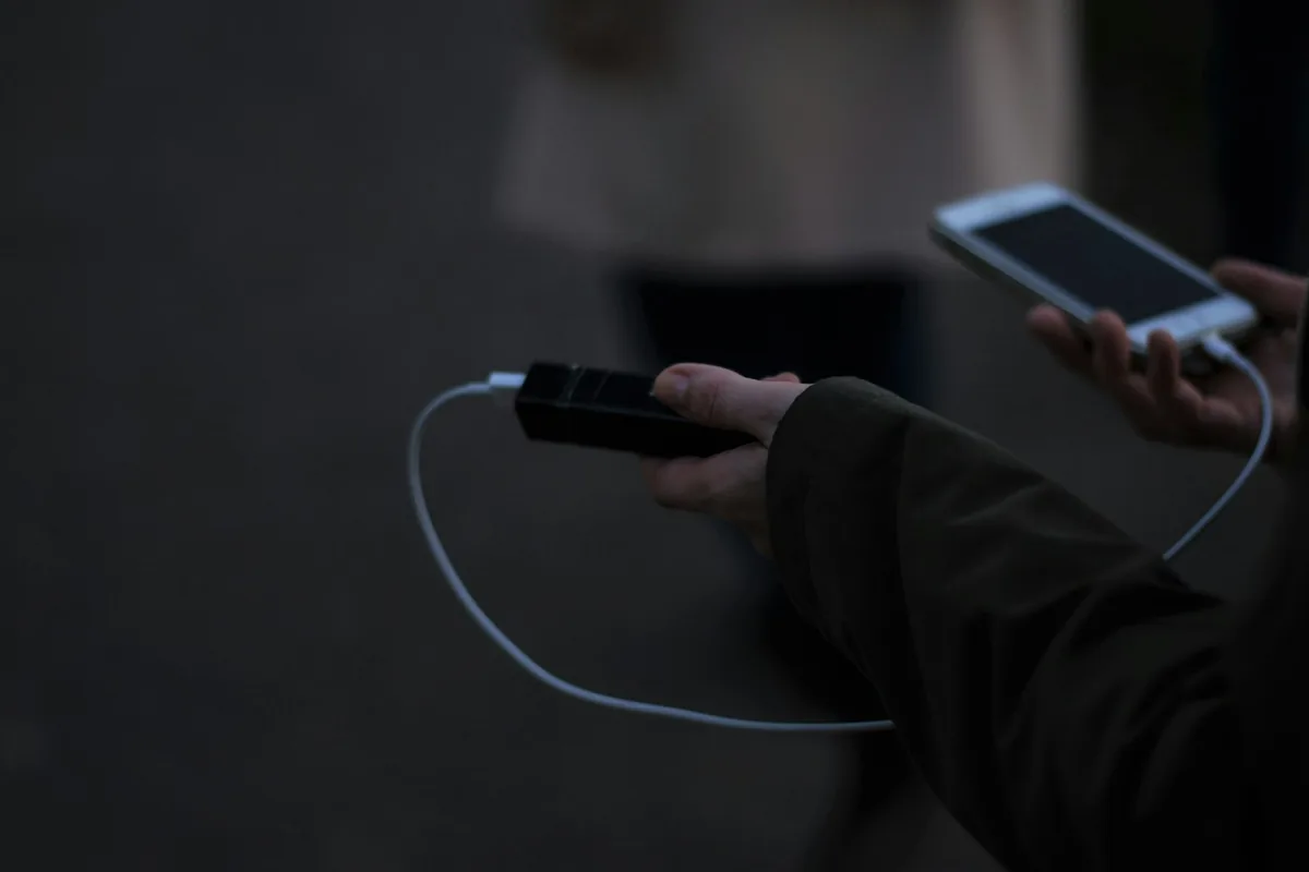 A hand holding a phone connected to a charging cable in a dark room