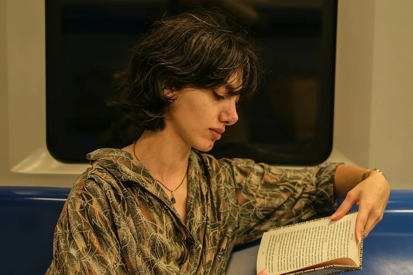 A person with dark hair reading an open book on a blue train seat