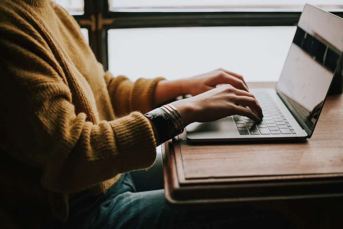 Person typing on a laptop next to a window