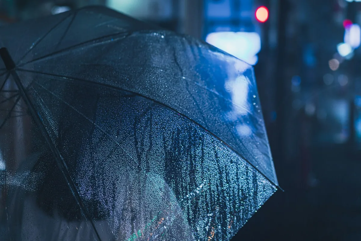 A person holding an umbrella on a rainy city street at night in blue light