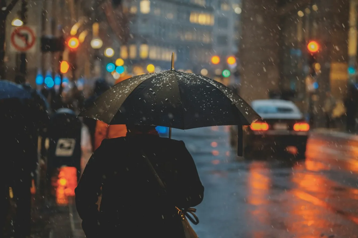 Een persoon met een paraplu op een regenachtige straat in de stad bij nacht, met vervaagde autolichten
