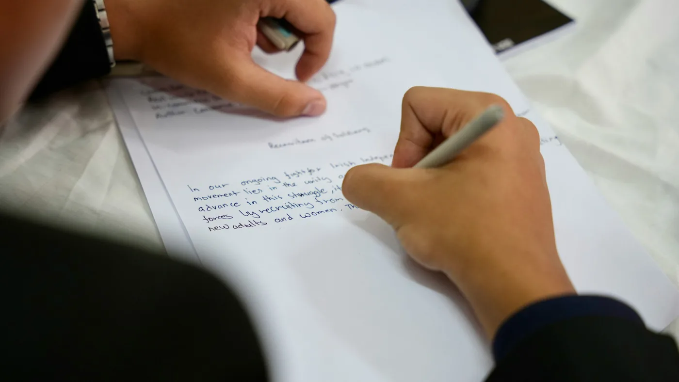 Person writing by hand on a sheet of paper on a desk