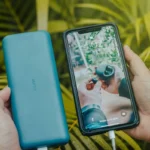 Hands holding a phone connected to a teal power bank