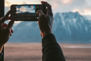 Two hands holding a phone to photograph a snowy mountain