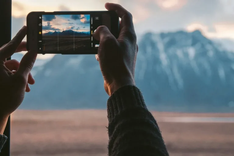 Two hands holding a phone to photograph a snowy mountain