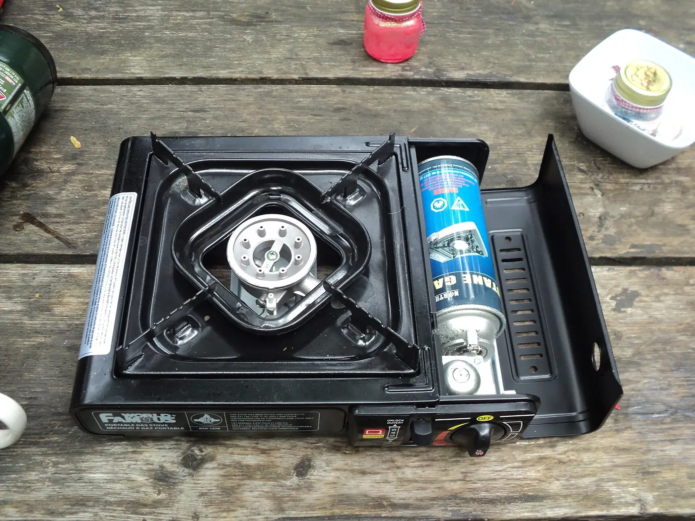 Cocina de camping de butano portátil, negra, con un cartucho de gas colocado, sobre una mesa de madera