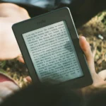 Manos sosteniendo un lector electrónico Kindle al aire libre, una comparación entre Kindle y Kobo para leer durante los viajes