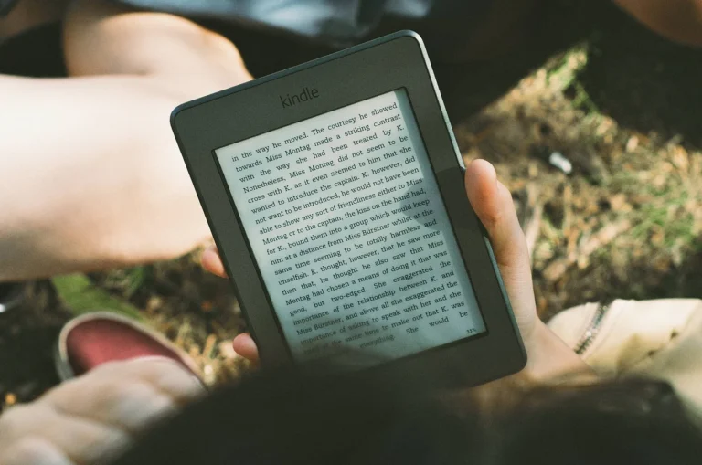 Hands holding a Kindle e-reader outdoors, a Kindle versus Kobo comparison for travel reading