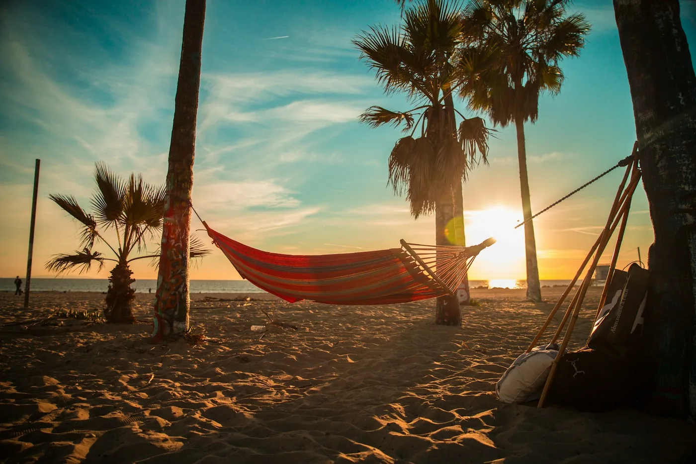 Red hammock on a sandy beach with palm trees and the sun low on the horizon