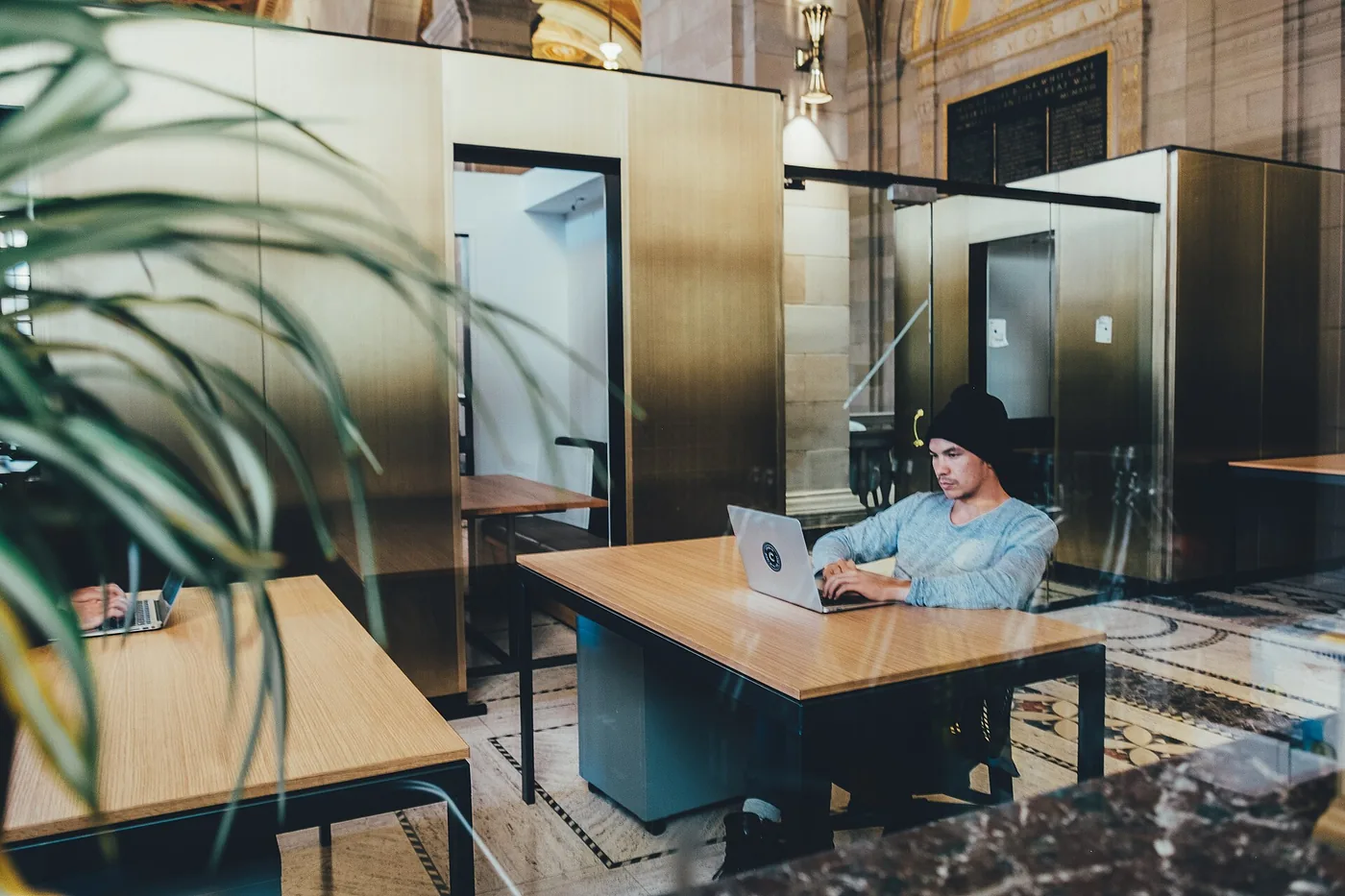 Remote worker with a laptop at a wooden desk in a large open workspace