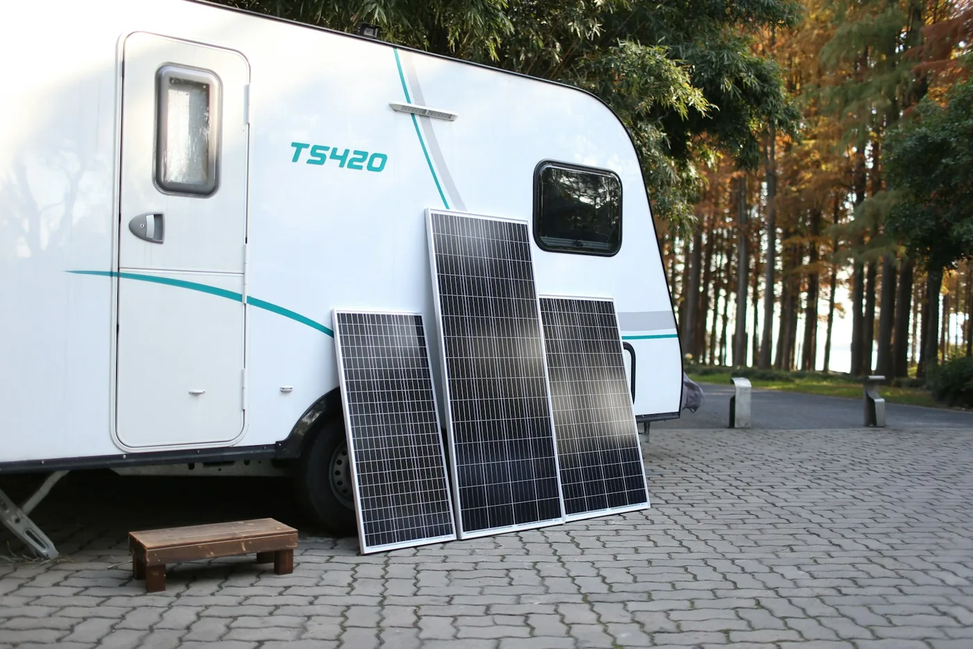 Drei starre, gerahmte Solarpanels, die an der Seite eines weißen Wohnwagens auf einer gepflasterten Fläche lehnen