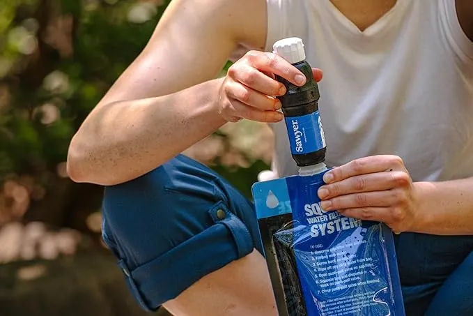 Hände schrauben einen Sawyer Squeeze Filter im Freien auf einen blauen Sawyer-Quetschbeutel