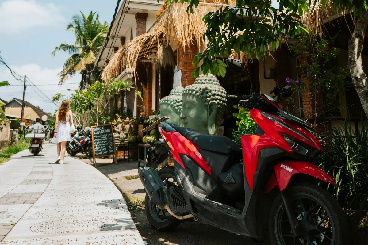 Red scooter parked on a path beside a stone statue in Ubud, scooter insurance in Bali