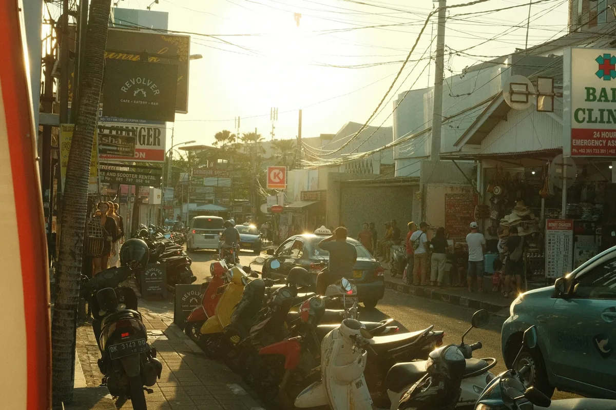 Busy Seminyak street with parked scooters in low sun