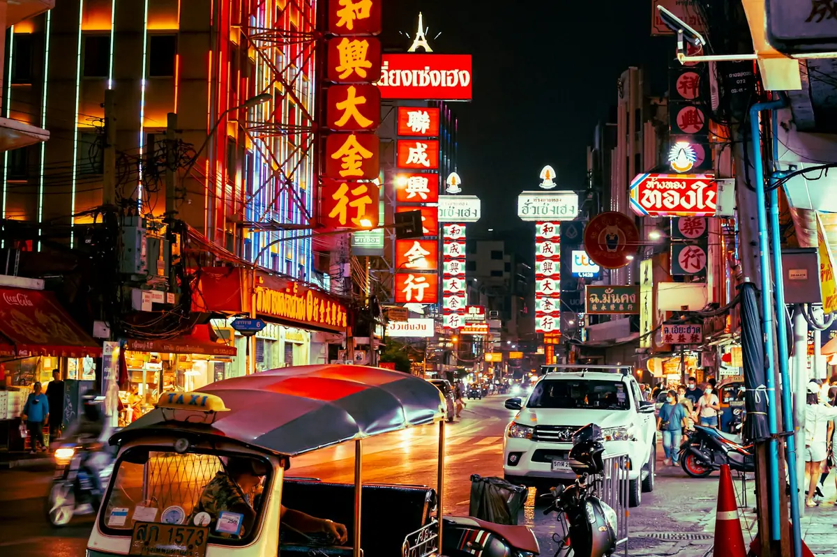 Neon-lit Chinatown street in Bangkok at night with a tuk-tuk in the foreground, scooter rental in Thailand