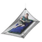 Sea to Summit Mosquito Pyramid Net opgehangen boven een blauwe mat, met een lezende vrouw erin