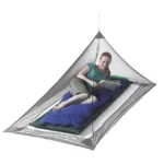 Sea to Summit Nano Mosquito Pyramid Net opgehangen boven een blauwe mat, met een lezende vrouw erin