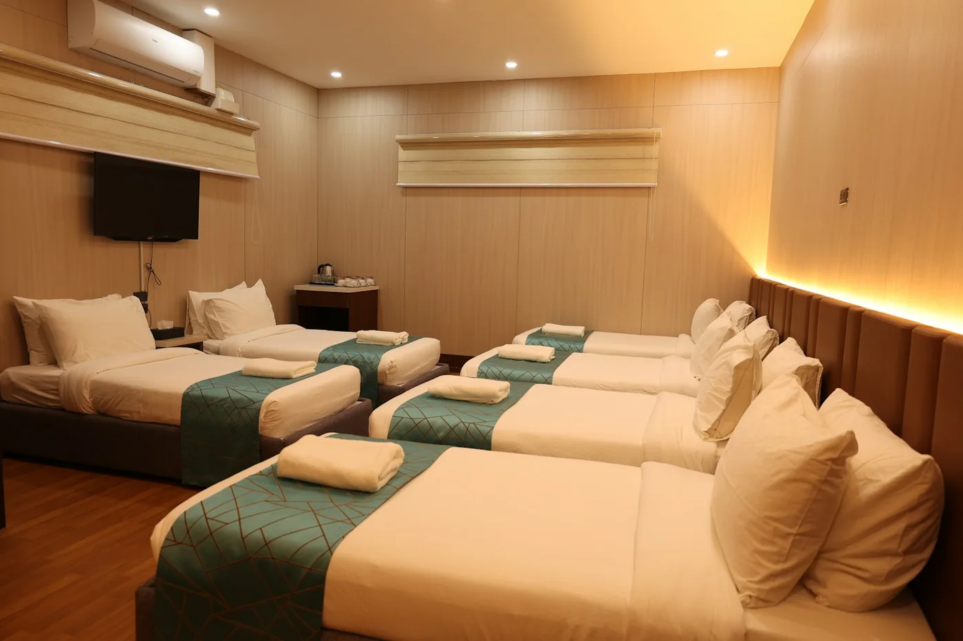 Shared hostel room with several beds made up with white linen and folded towels under warm ceiling lights