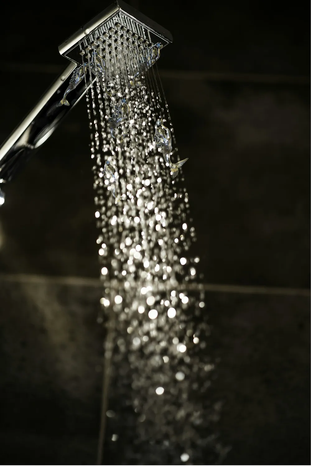 A shower head with water drops falling against a dark background