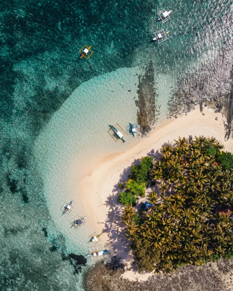 Aerial view of Guyam Island off Siargao with outrigger boats on the white sand beach