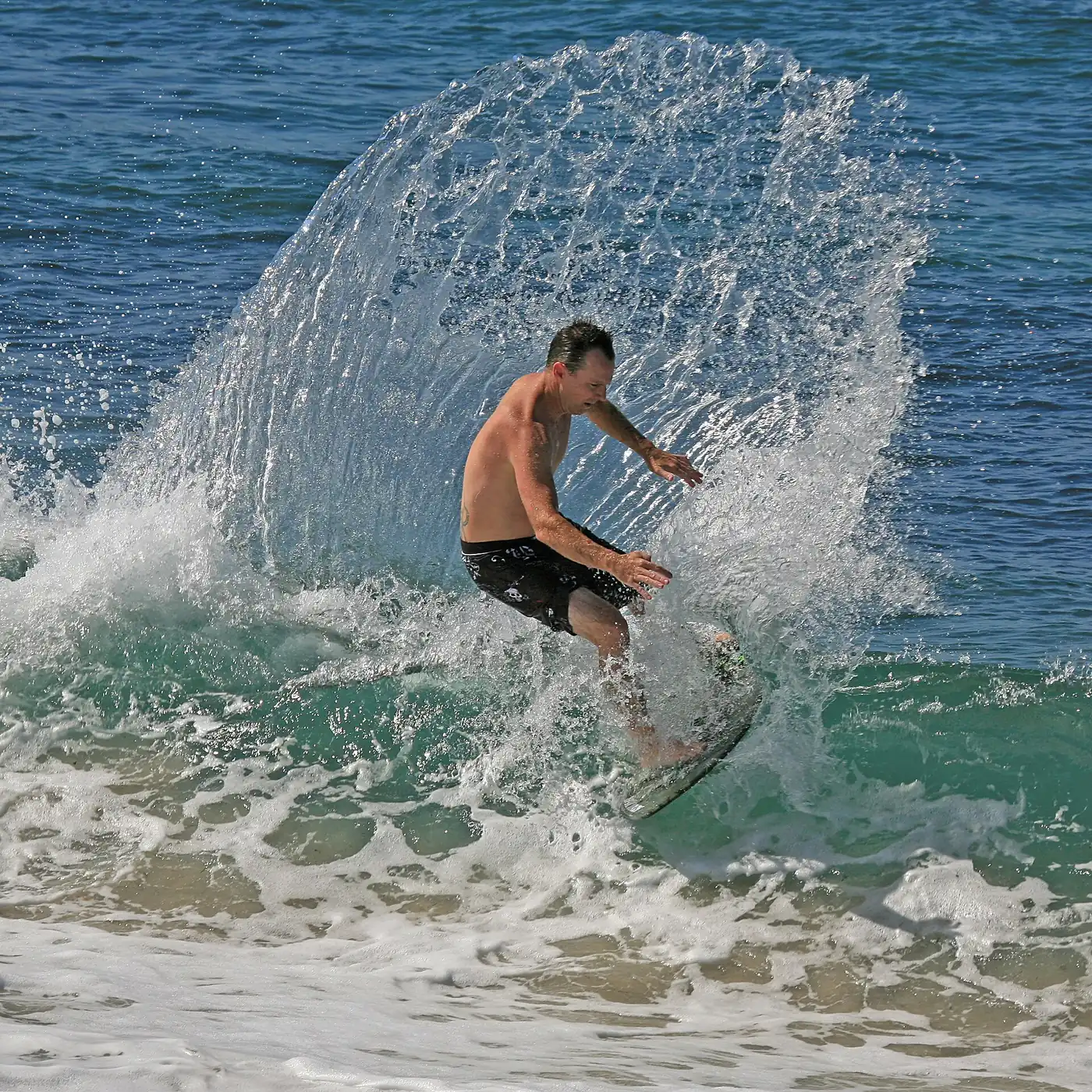 Skimboarder spraying water on a wave in San Diego, California