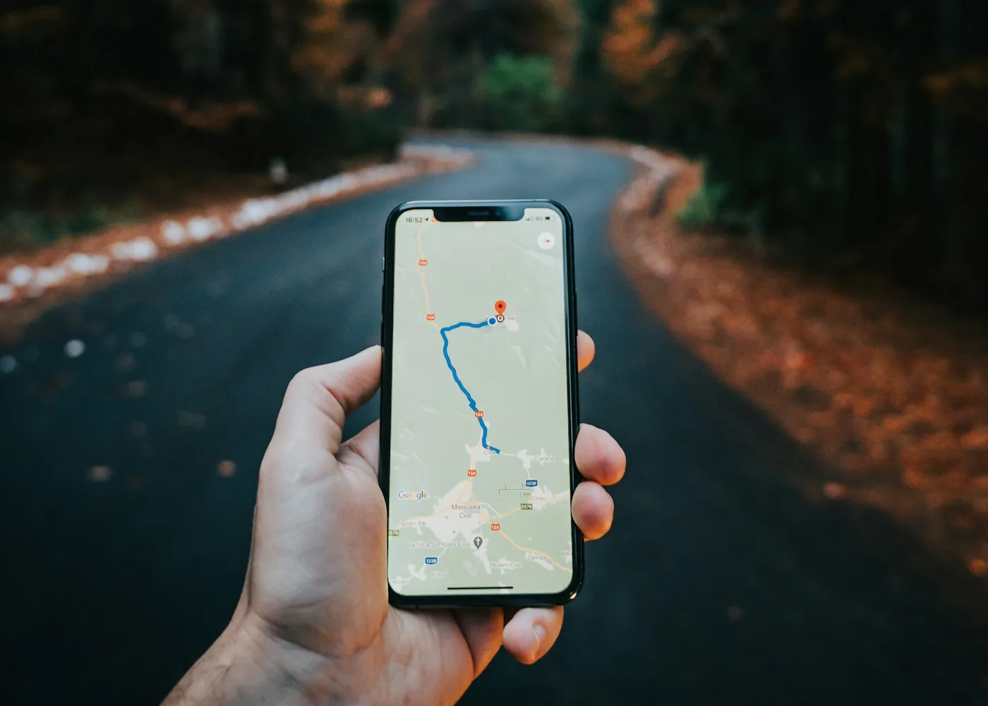 Hand hält ein Smartphone, das eine Navigationskarte auf einer Waldstraße zeigt