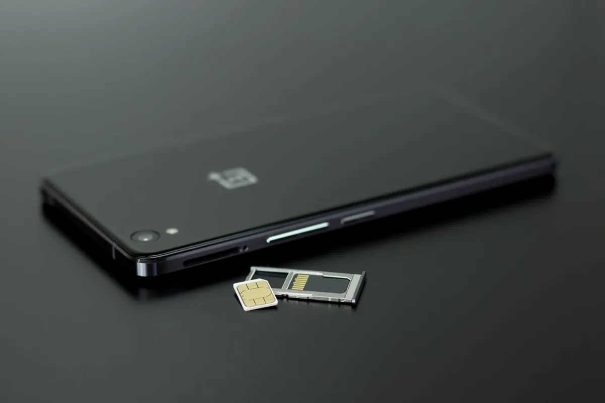 Smartphone lying on a dark table next to its SIM card tray and SIM cards