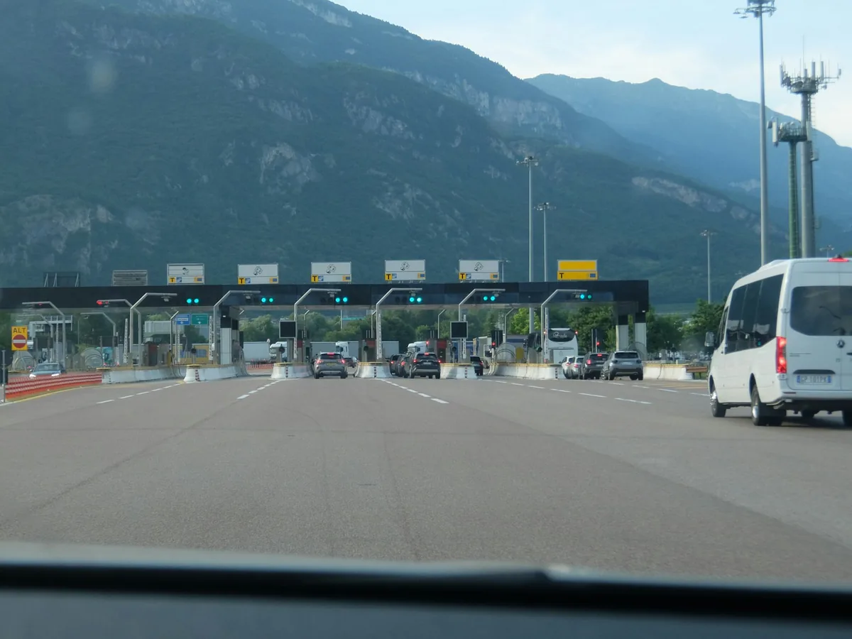 Cars approaching a multi-lane toll plaza with mountains behind, toll roads when renting a car