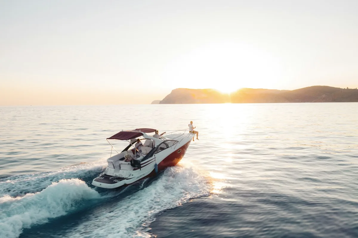 Een speedboot die bij zonsondergang over open zee vaart, met een heuvelachtige kust in de verte