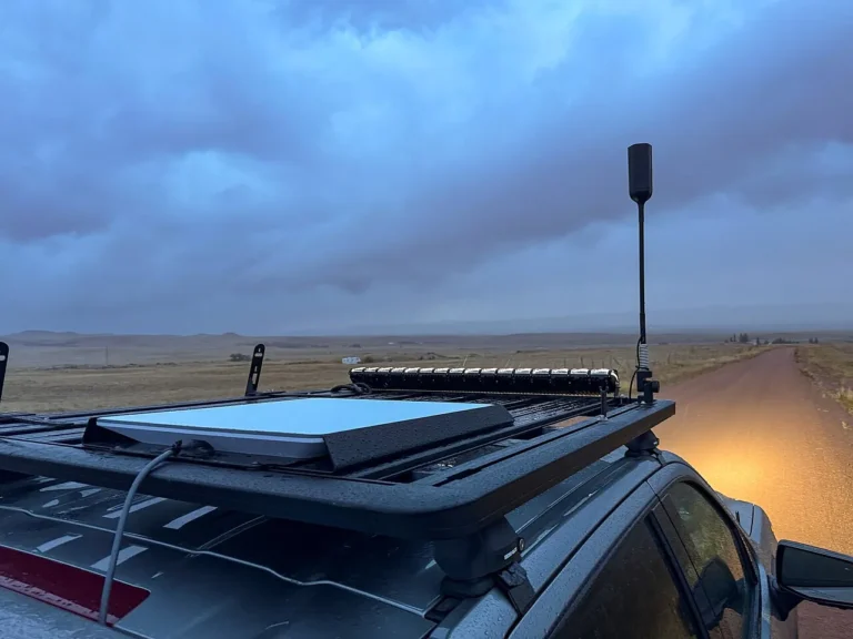 Starlink flat panel dish on a vehicle roof rack under a stormy sky on a dirt road