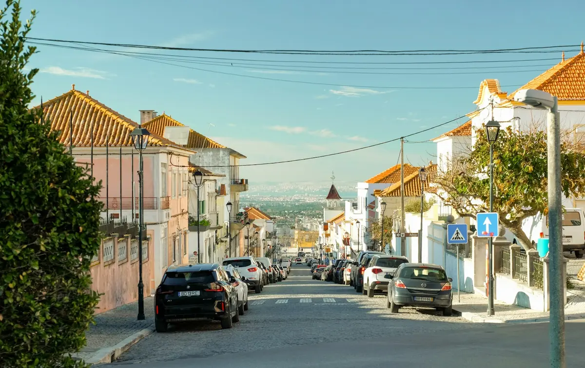 Street lined with parked cars below pastel buildings