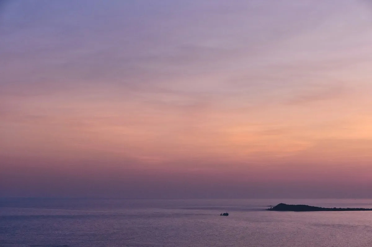 Pink and purple sunset sky over the sea with a small boat and an island on the horizon