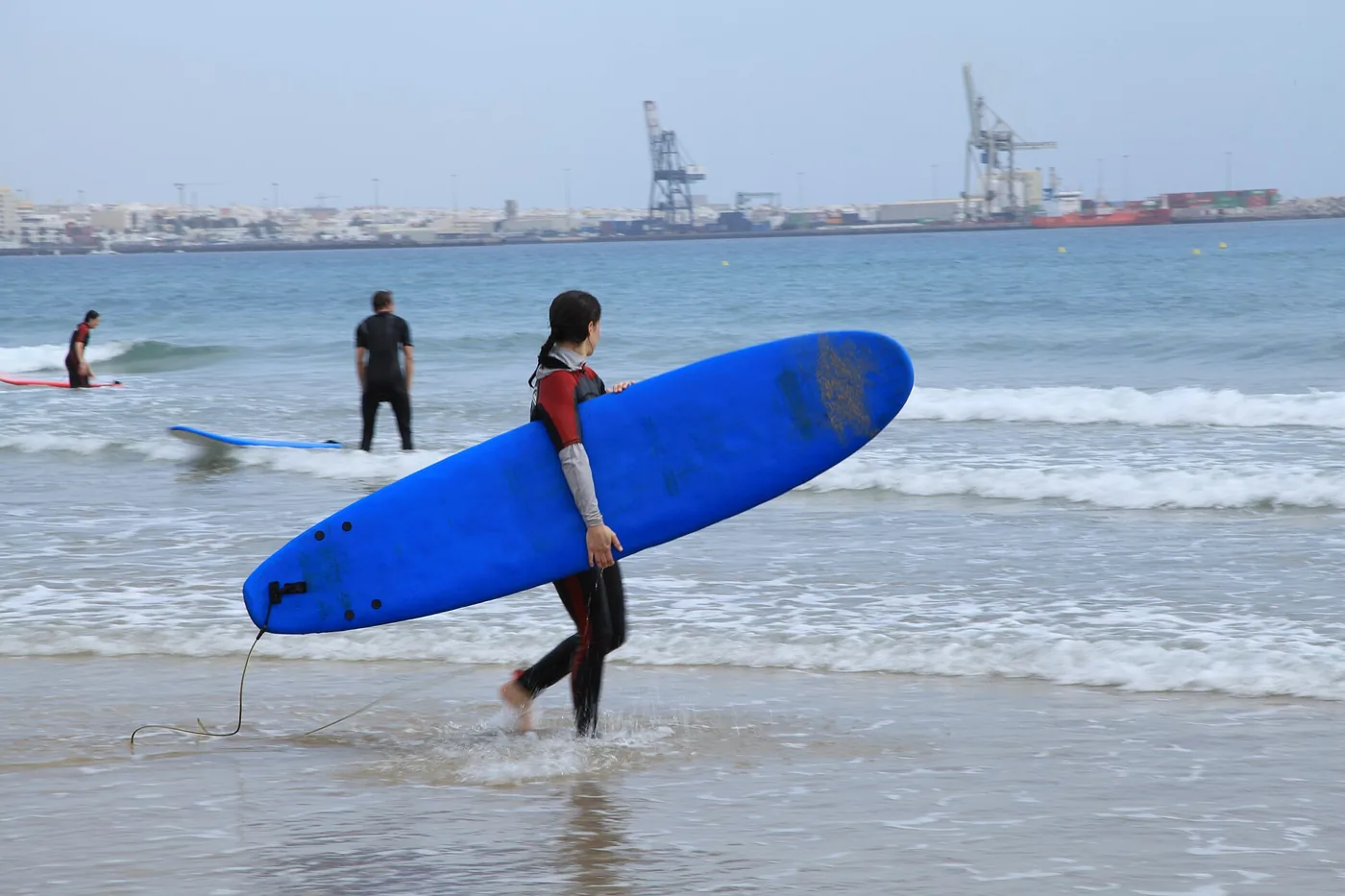 Surfer carrying a blue soft-top board into the sea at Playa Blanca, Fuerteventura