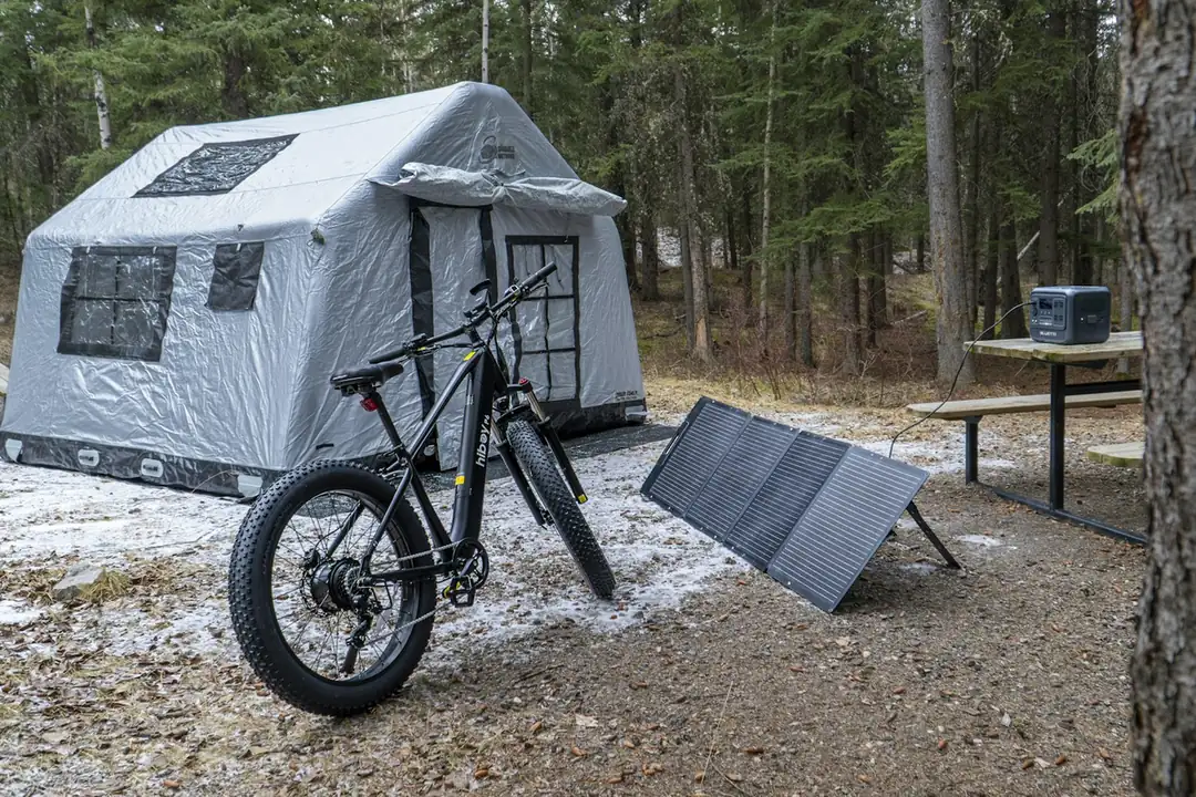 Grey tent, an e-bike and a folding solar panel at a forest campsite
