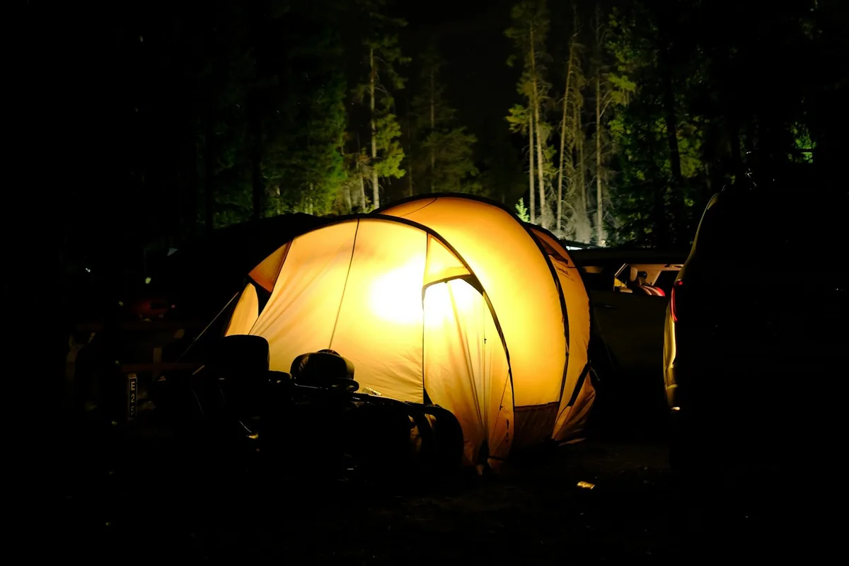 Een tent verlicht van binnenuit 's nachts tussen hoge bomen