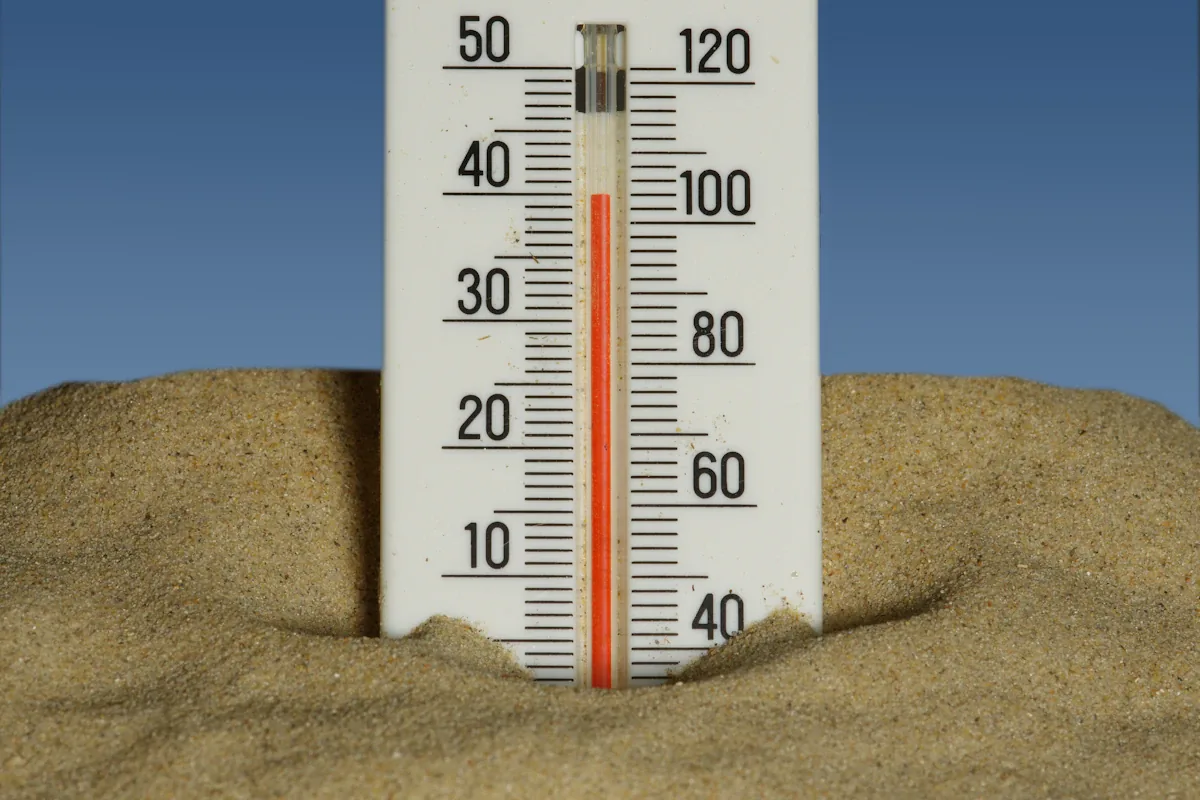 Een thermometer die in het zand staat onder een blauwe lucht en een hoge temperatuur aangeeft