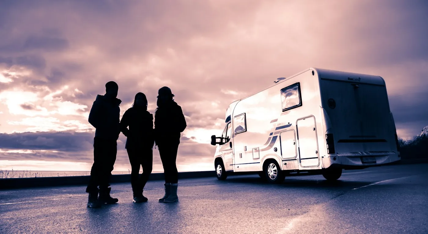Three people in silhouette standing beside a white motorhome at dusk