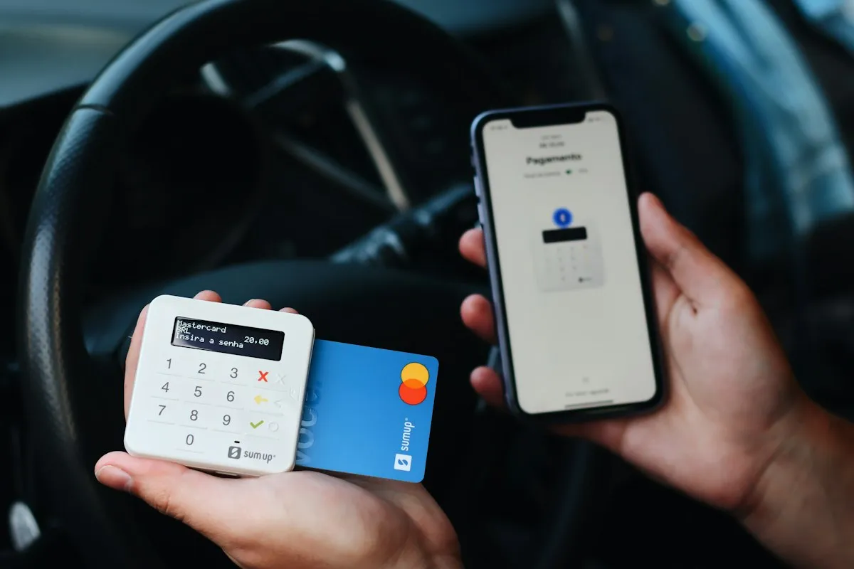 Hand holding a bank card next to a phone with a card reader, paying with a travel card abroad