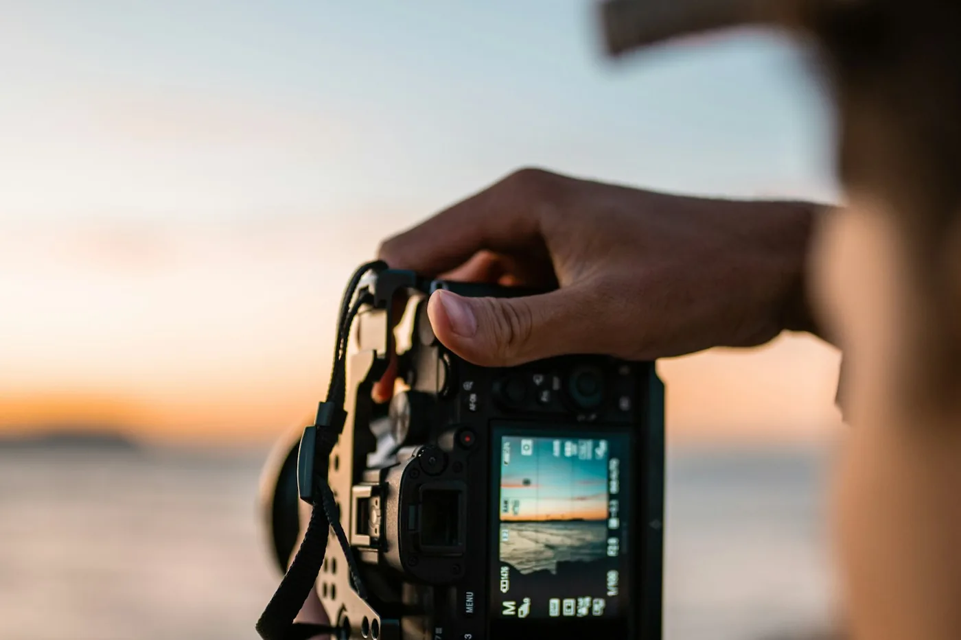 Photographer holding a black camera up to take a picture of a sunset over the sea