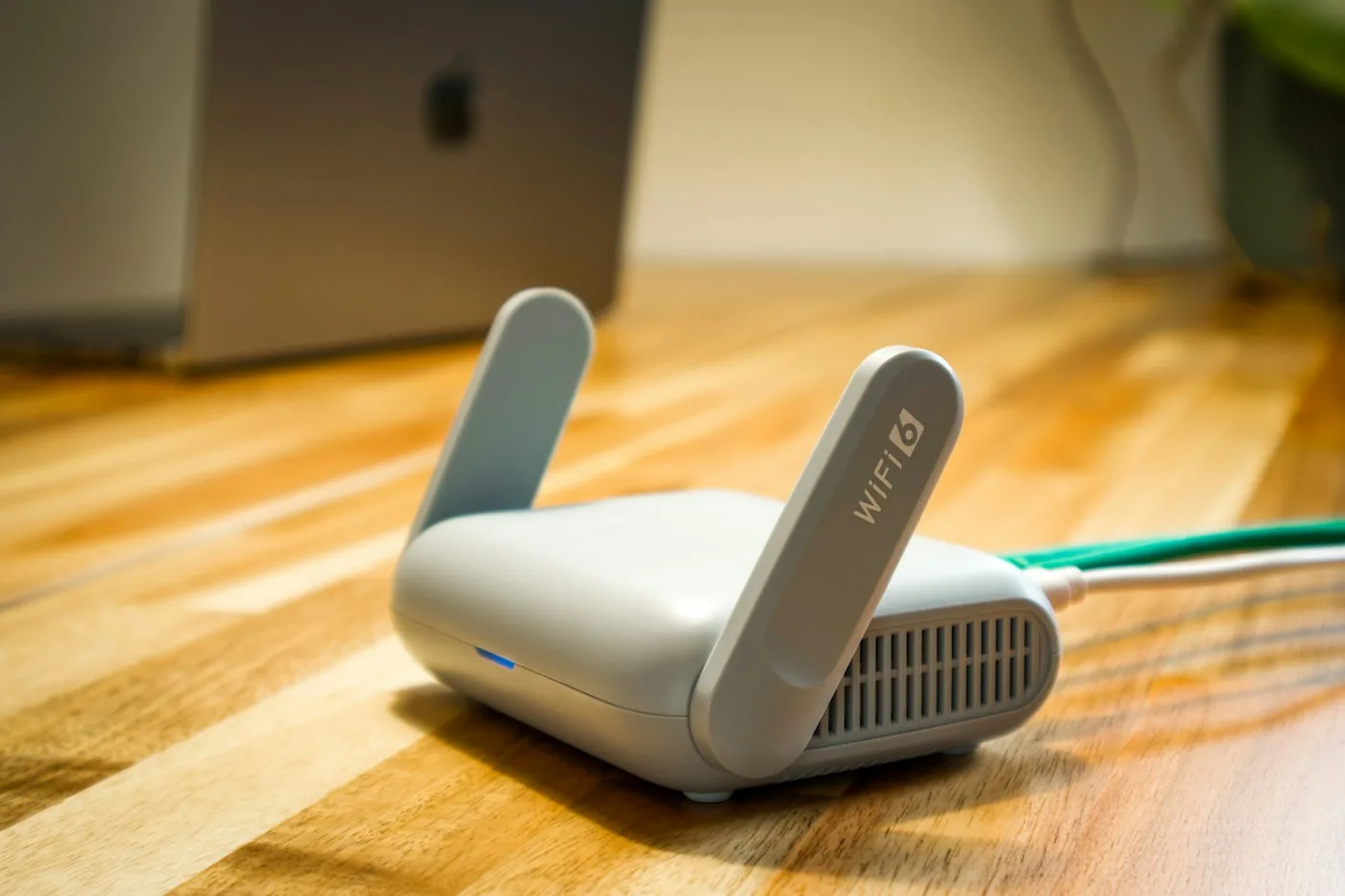 Small white travel router with two folded antennas on a wooden table in front of a laptop