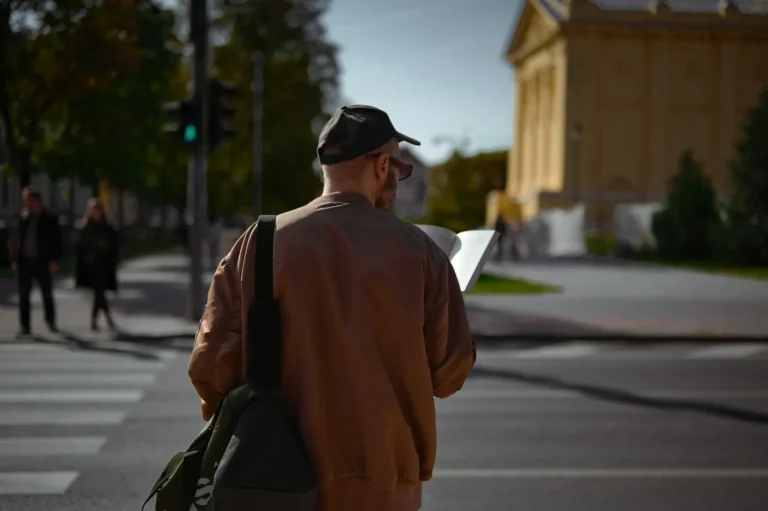 Traveler with a backpack seen from behind reading a map at a street crossing