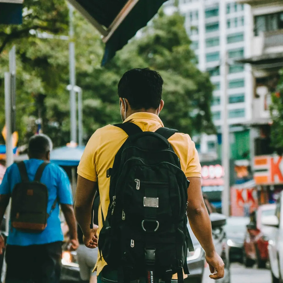 Traveler seen from behind carrying a black backpack along a busy city street