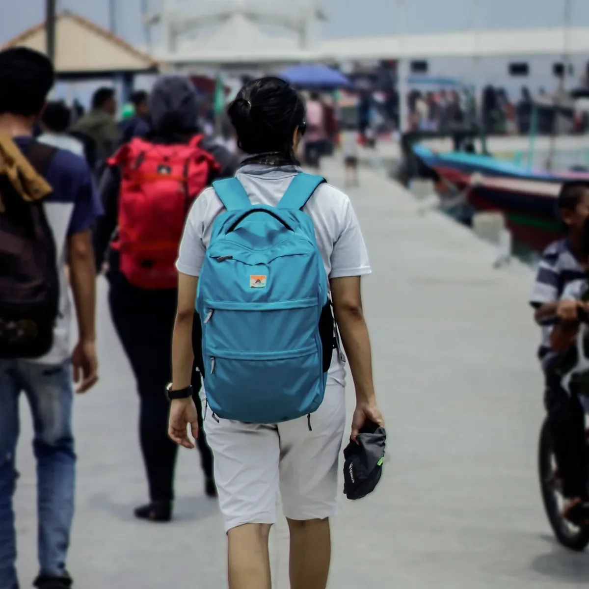 Traveler with a blue backpack walking along a pier among other people