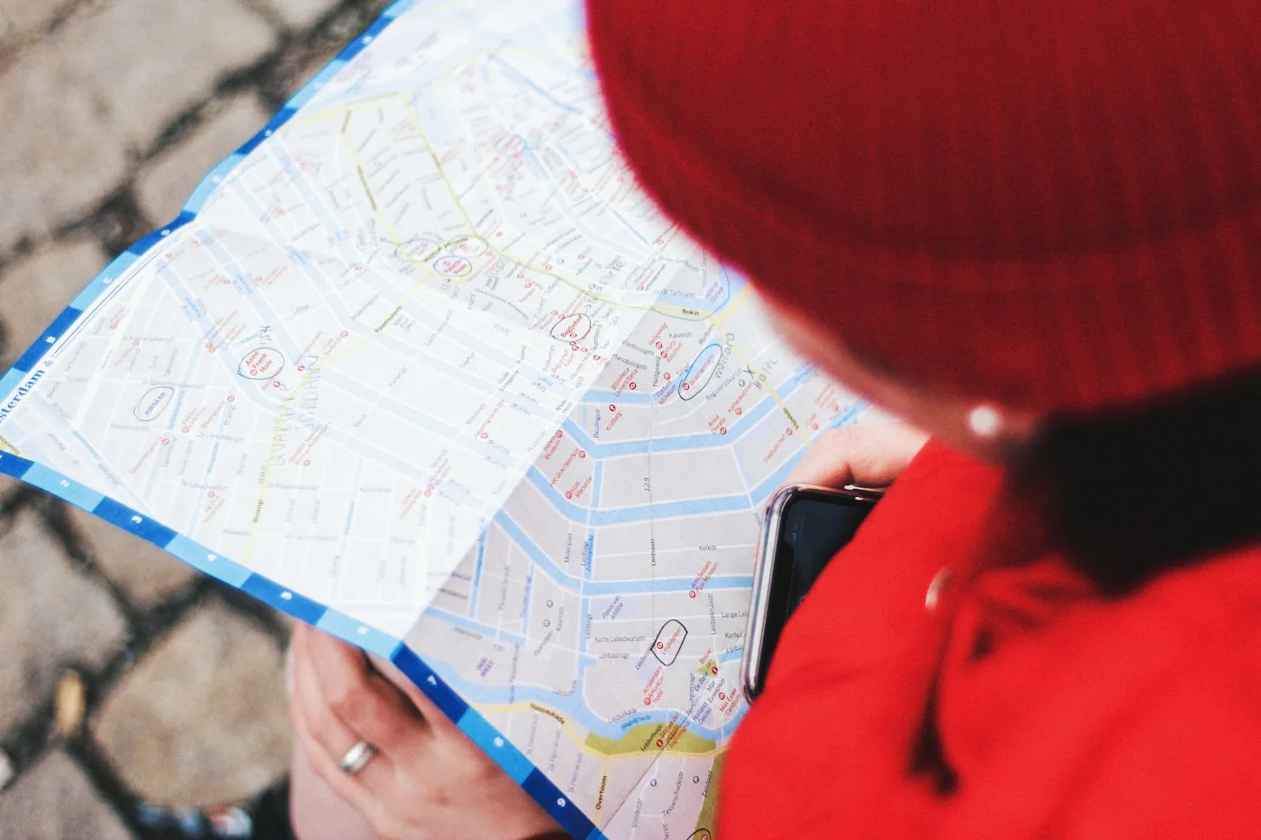 Traveler in a red beanie and jacket holding a paper city map and a phone