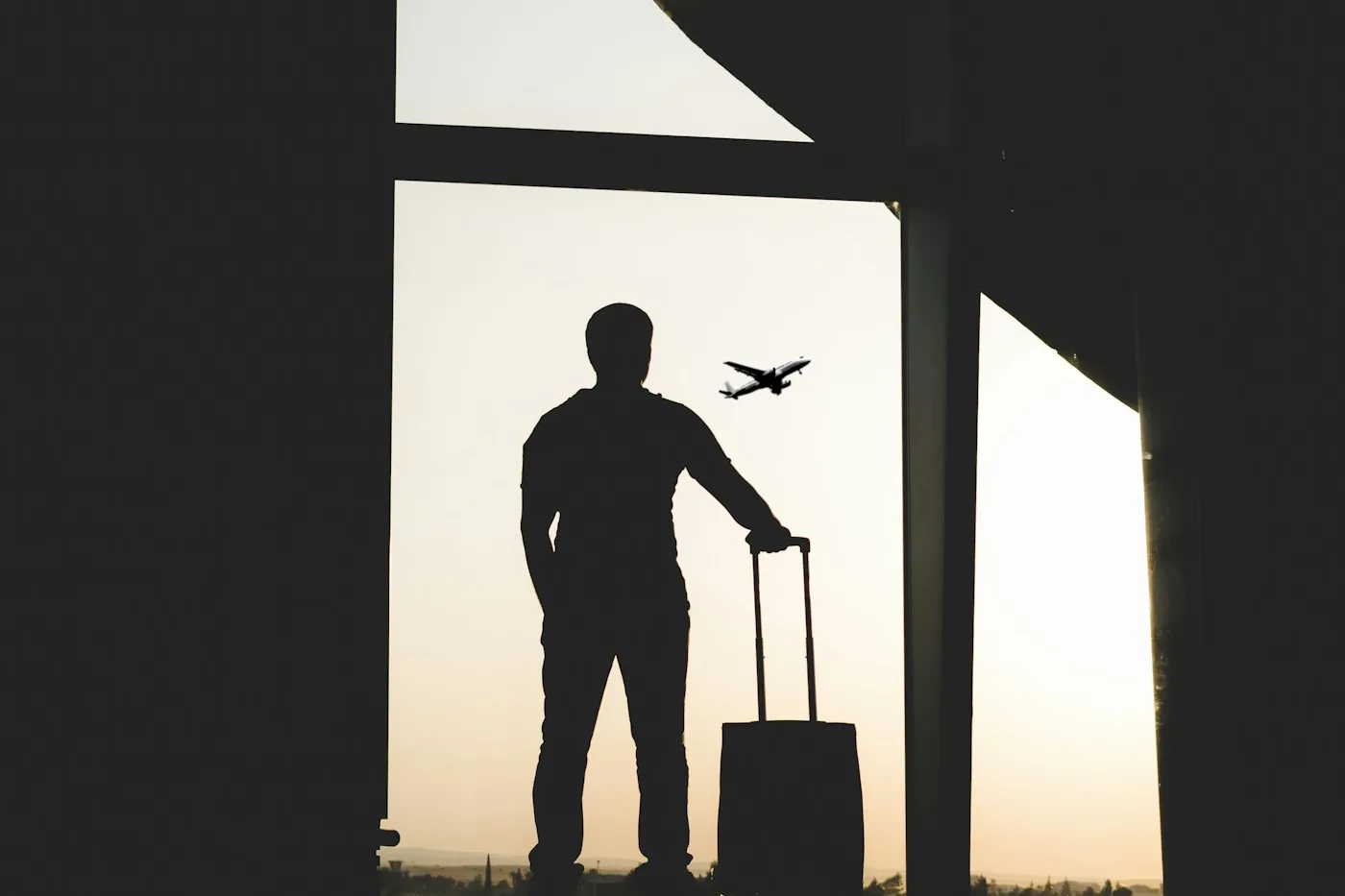 Silhouette of a traveler with a suitcase at an airport window with a plane outside