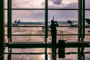Silhouette of a traveler with a suitcase photographing planes through a tall airport window at dusk